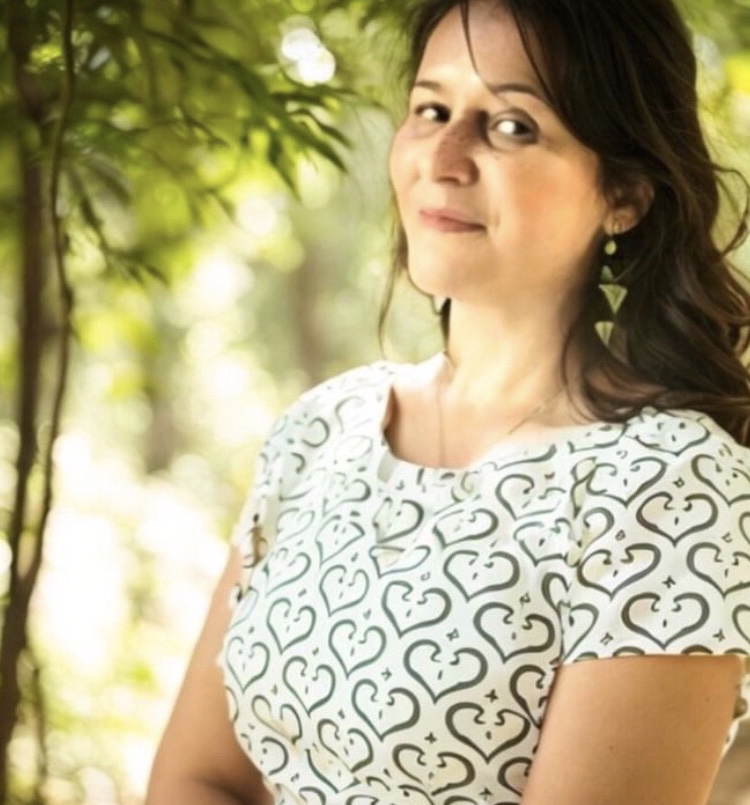 Patrícia Scarletti de blusa branca estampada, em um jardim com folhagens ao fundo